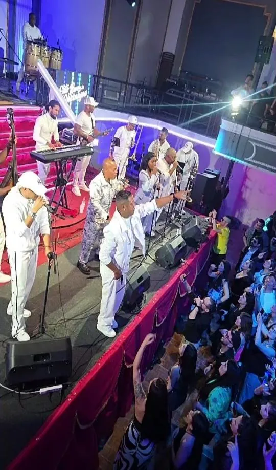 Orquesta cubana vestida de blanco tocando en un escenario frente al público